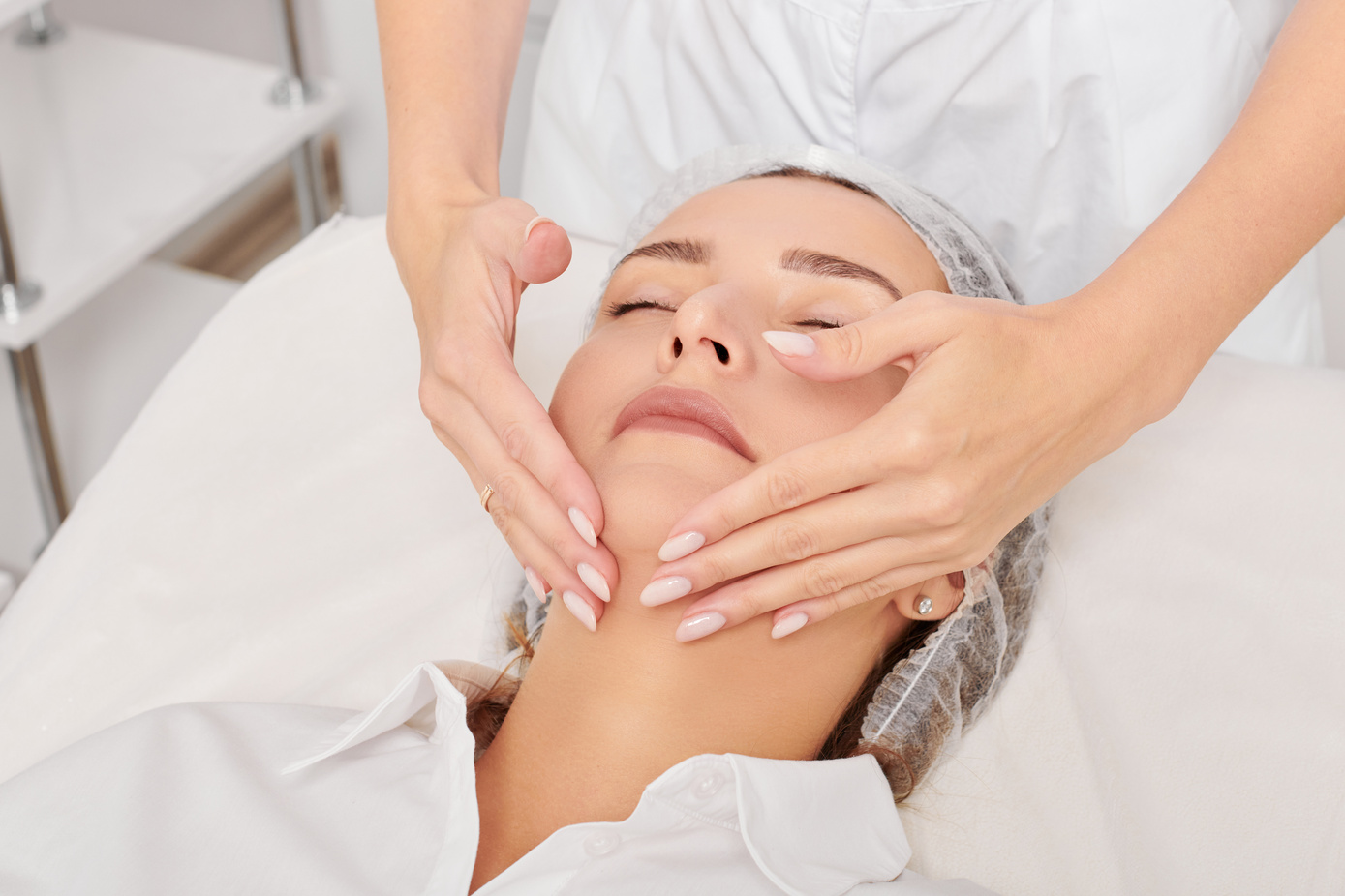 Beautician massages woman face skin after rubbing moisturizing cream for rejuvenation in clinic